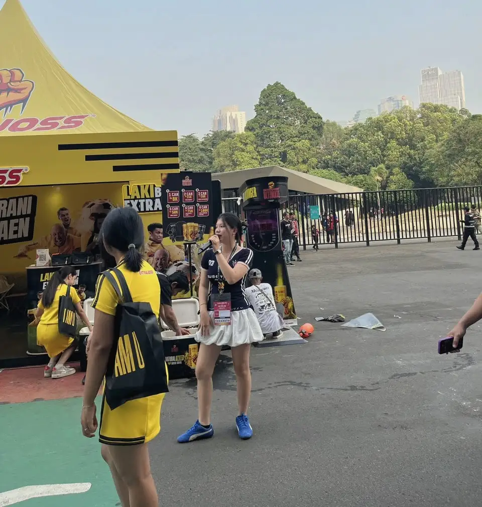 A host with a microphone leads an activation beside a branded booth and game machine