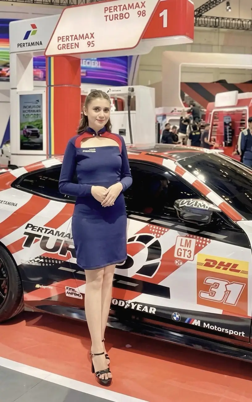 A brand ambassador in a fitted navy dress beside a race car at an auto show booth