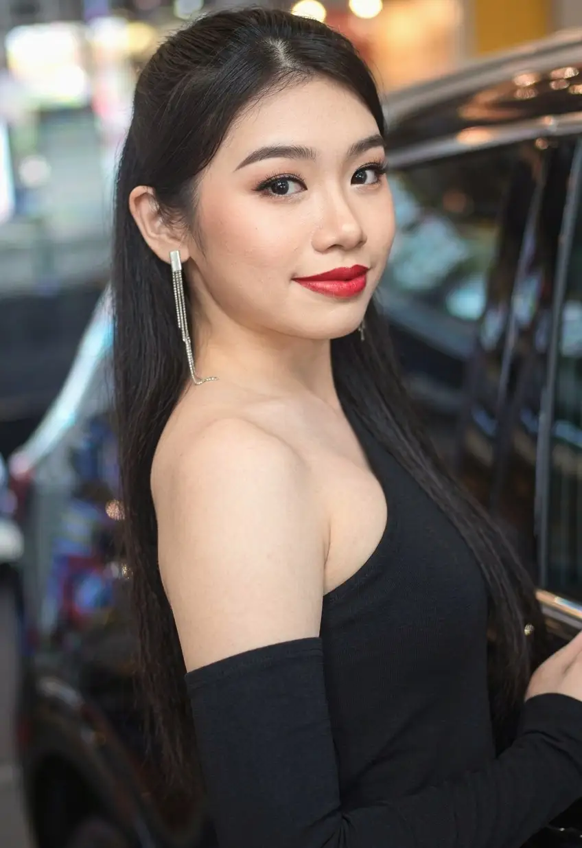 Portrait of a model in a black off-shoulder top with long earrings beside a vehicle at an auto show