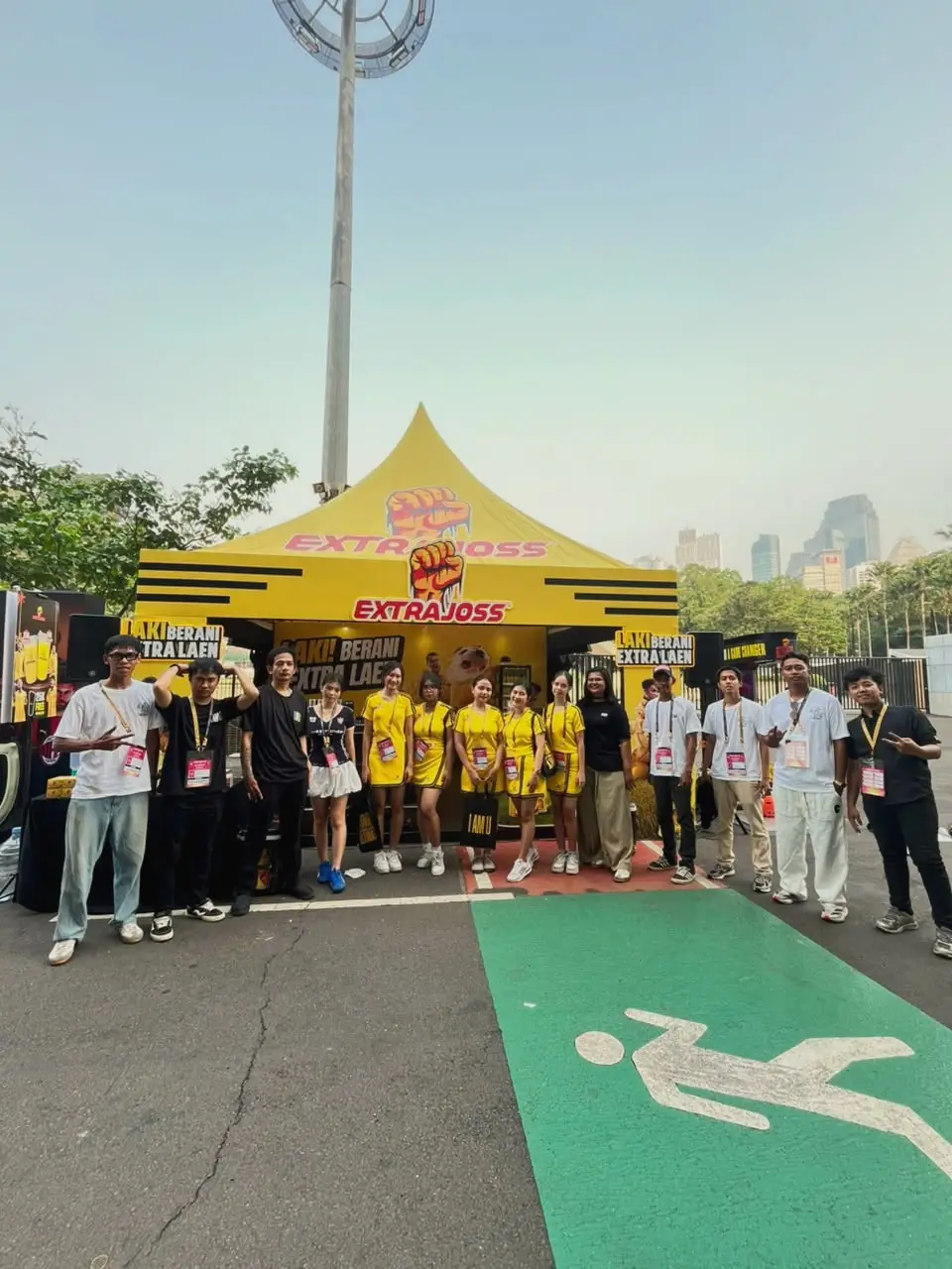 Tim aktivasi berisi brand ambassador dan kru di depan tenda brand berwarna kuning di luar stadion