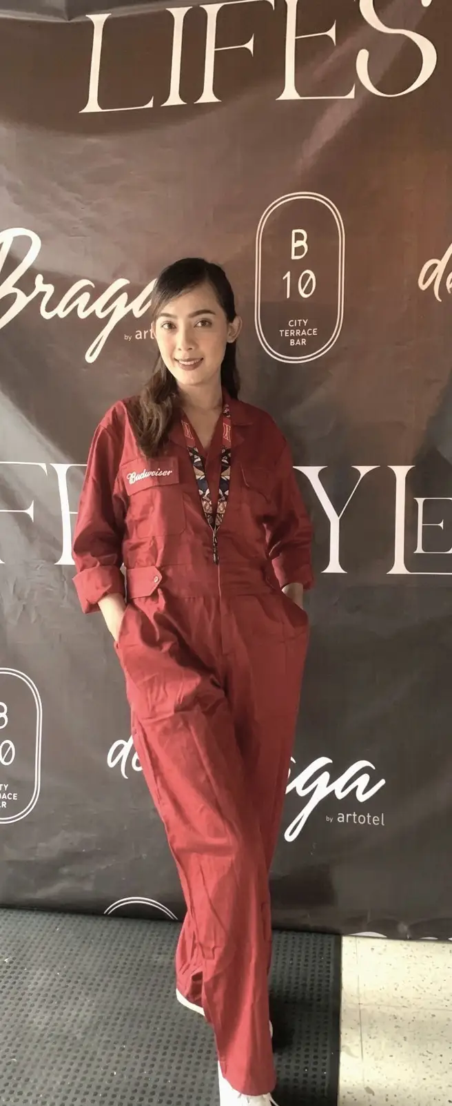 A brand ambassador in a red brand jumpsuit in front of a venue backdrop
