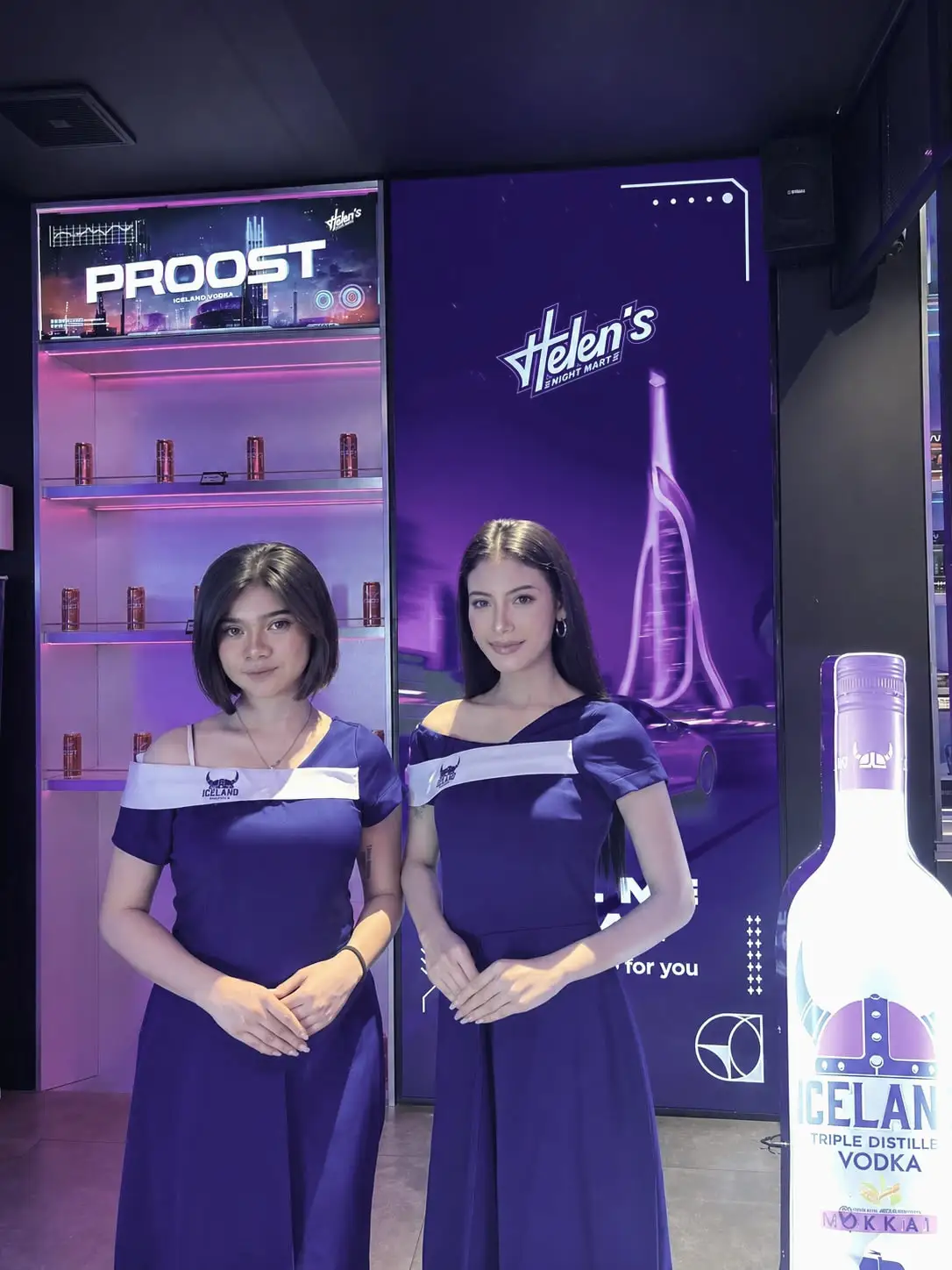 Two brand ambassadors in blue dresses beside an illuminated product display