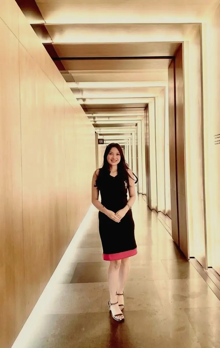 A hostess in a black dress standing at the end of a long, warmly lit corridor