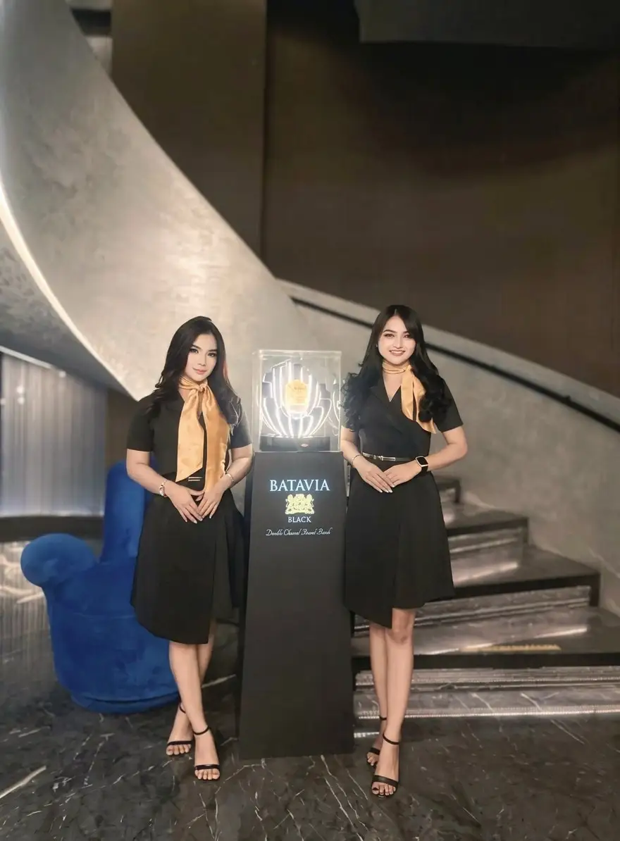 Dua brand ambassador berbusana hitam dengan syal emas mengapit display produk yang menyala