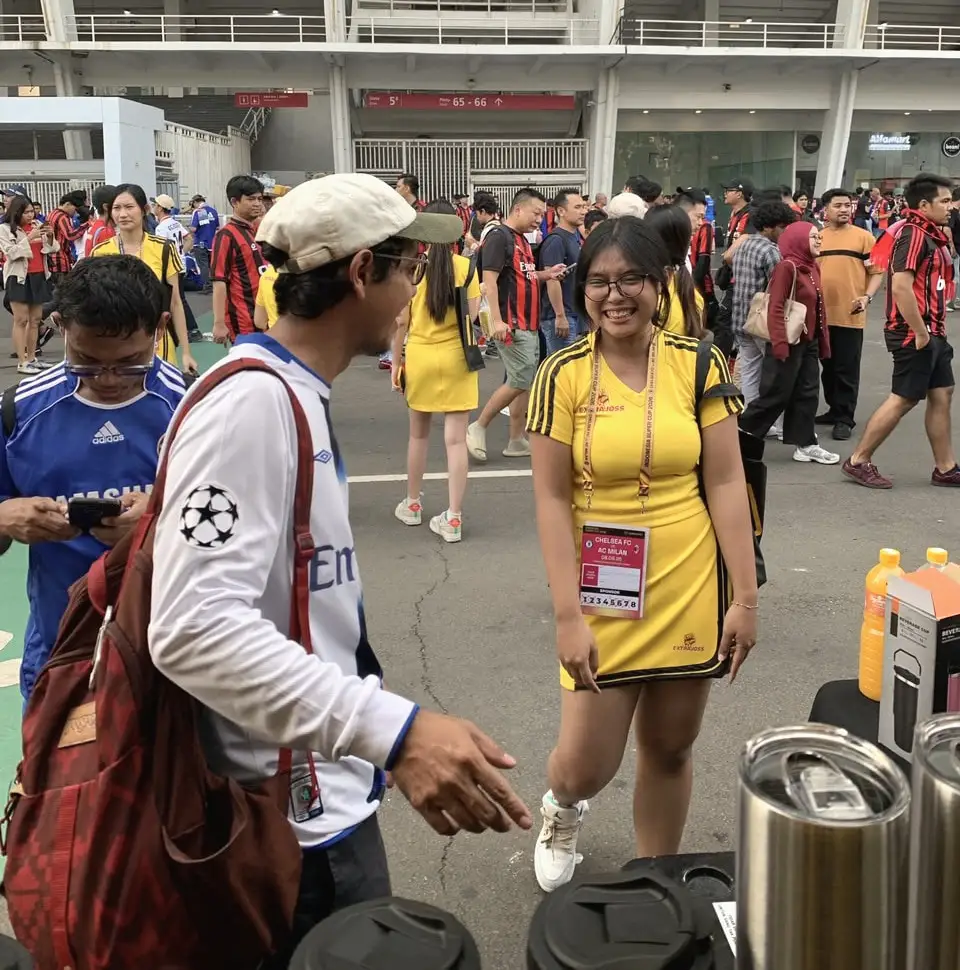 Brand ambassador berseragam kuning tersenyum menyapa pengunjung di titik sampling stadion