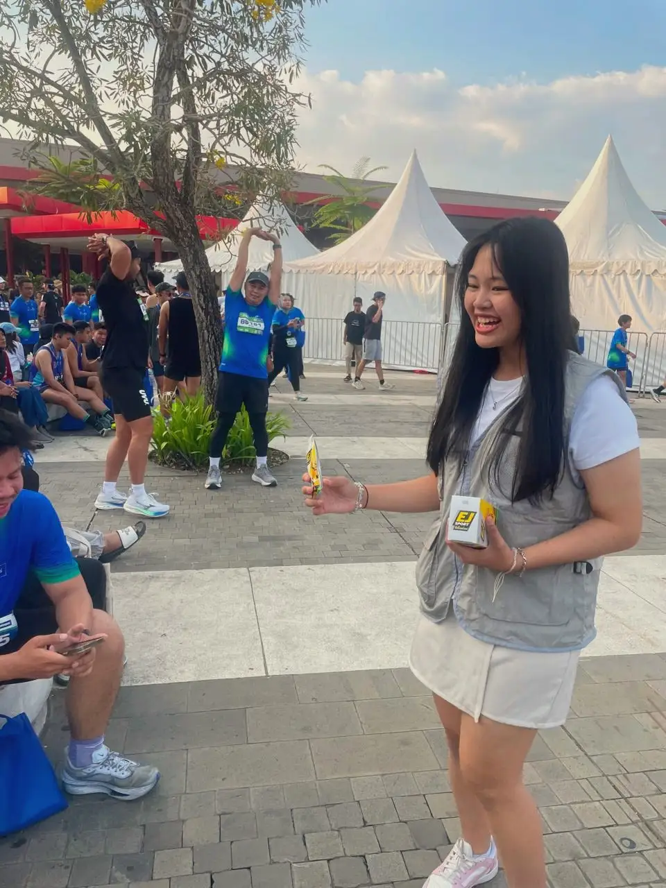 Seorang brand ambassador tertawa sambil menawarkan sampel produk kepada pelari usai lomba