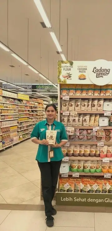 A retail promoter in a green uniform beside a product display in a supermarket aisle
