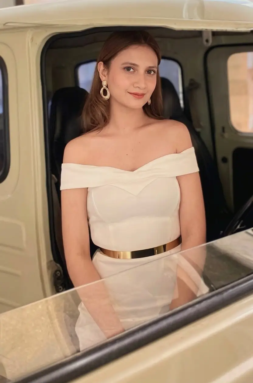 A model in an off-shoulder white dress seated inside a vehicle on display