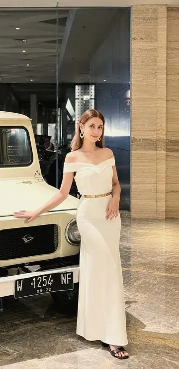 A brand ambassador in a white gown beside a classic vehicle on display