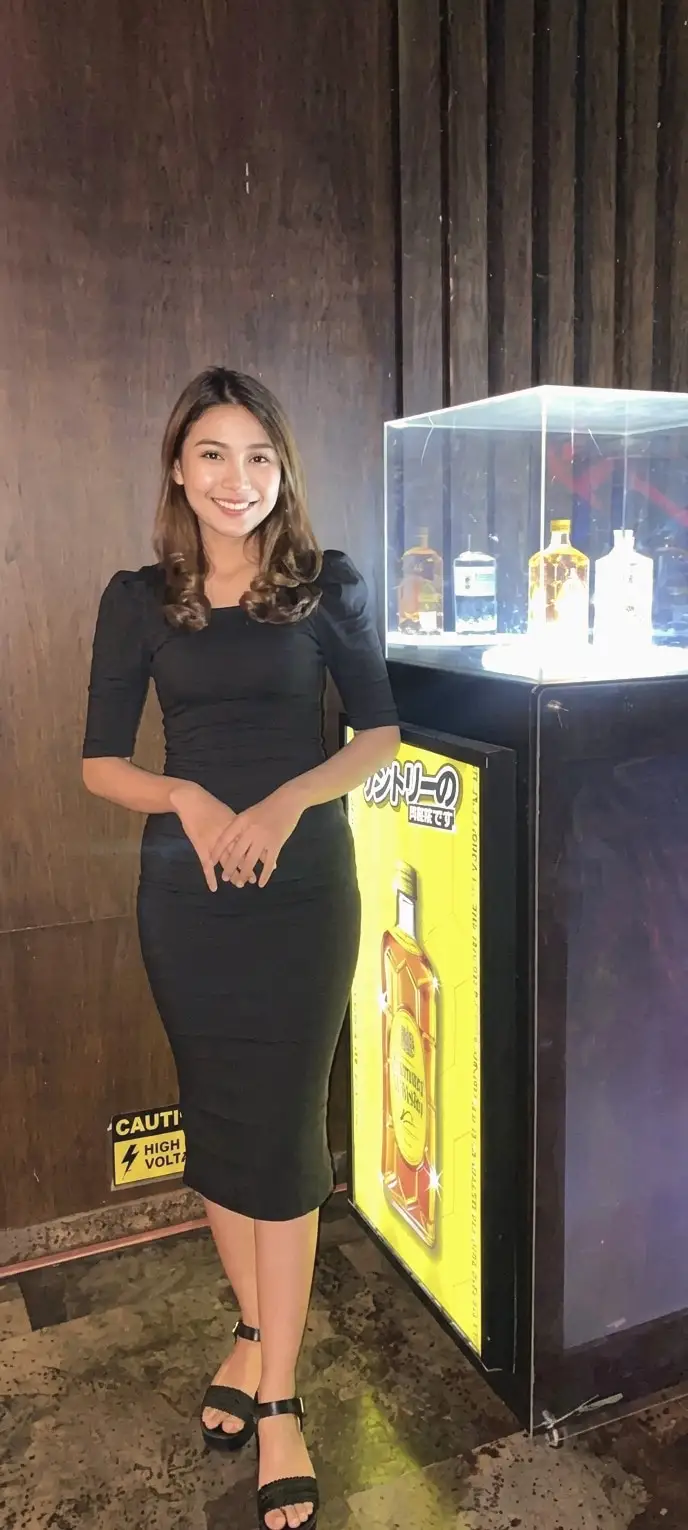 A brand ambassador in black beside an illuminated whisky display case